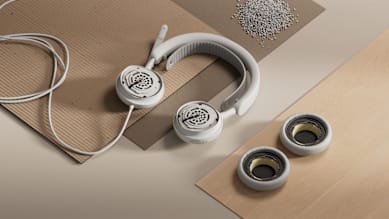 Logitech Zone Wired 2 for Business Headset in Weiß mit abgenommenen Ohrpolstern und Komponenten, platziert auf Karton- und Holzoberflächen mit Materialien.
